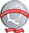 Round silver medal with white writing and a red banner and ribbon.