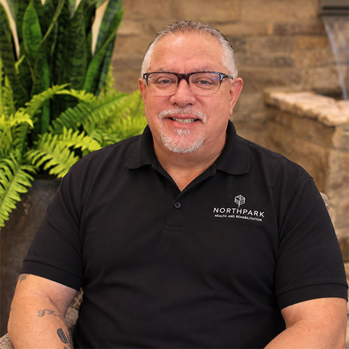 Smiling man with trimmed goatee wearing glasses and a short-sleeved polo shirt.