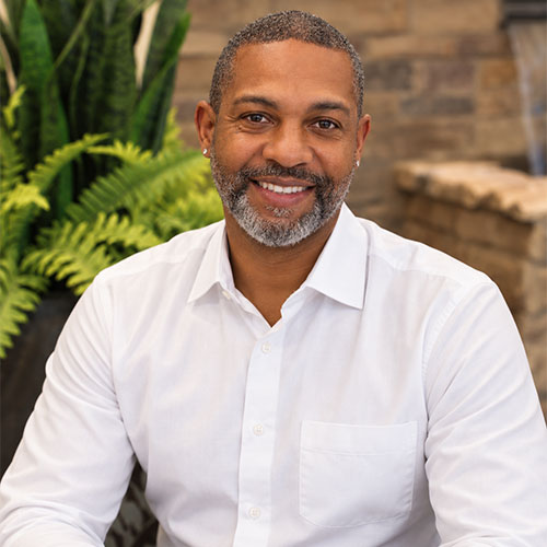 Smiling man with short hair and a well-trimmed beard and moustache wearing a white button down dress shirt.