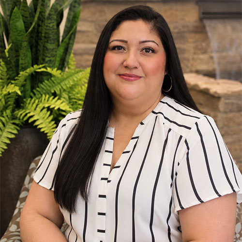 Slightly-smiling woman with long dark straight hair wearing short sleeved striped business shirt.
