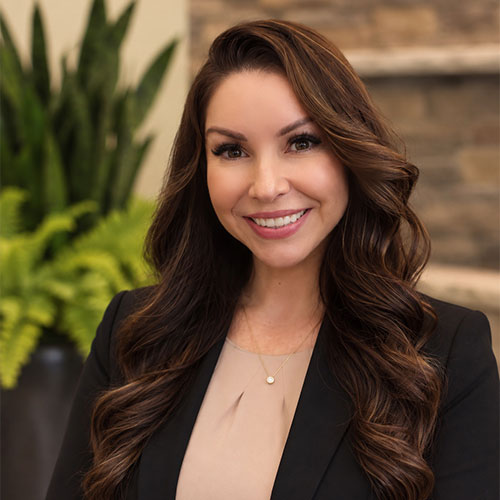 Smiling woman with long, dark, wavy hair wearing a business jacket.
