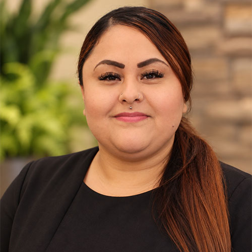 Slightly smiling woman with her long hair in a ponytail pulled over her left shoulder. She is wearing a business top and jacket.